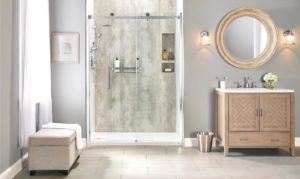 New walk-in shower with stone-patterned walls. Light gray bathroom with gold-framed mirror above sink